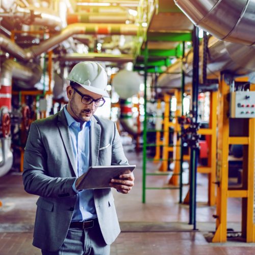 gerente-caucasico-guapo-traje-gris-casco-cabeza-usando-tableta-mientras-parado-planta-energia